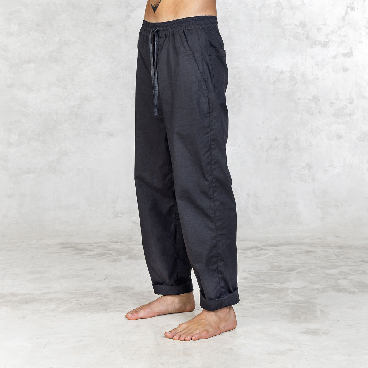 Person wearing Dagger Blamo pants, barefoot, shown from 3/4 view. The pants have a full elastic waist, drawstring, and front zipper pockets, with slightly tapered legs