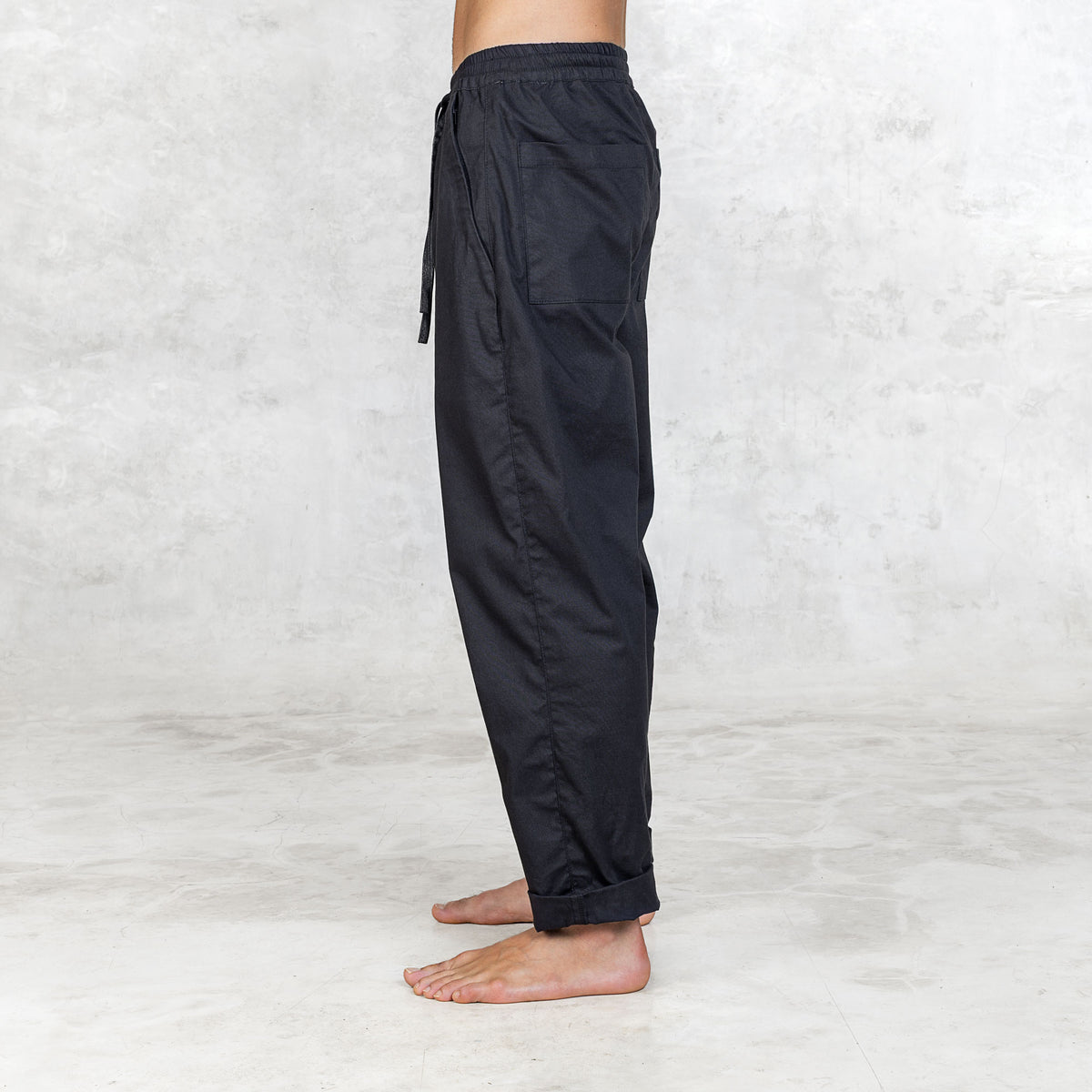 Person wearing Dagger Blamo pants, barefoot, shown from side view. The pants have a full elastic waist, drawstring, and front zipper pockets, with slightly tapered legs