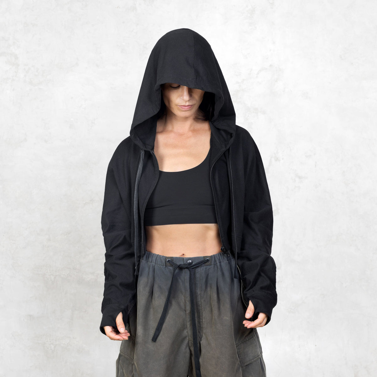 Model facing front from the waist up wearing unzipped black cropped French terry Daydreamer Hoodie with boxy fit and extra long arms. 

