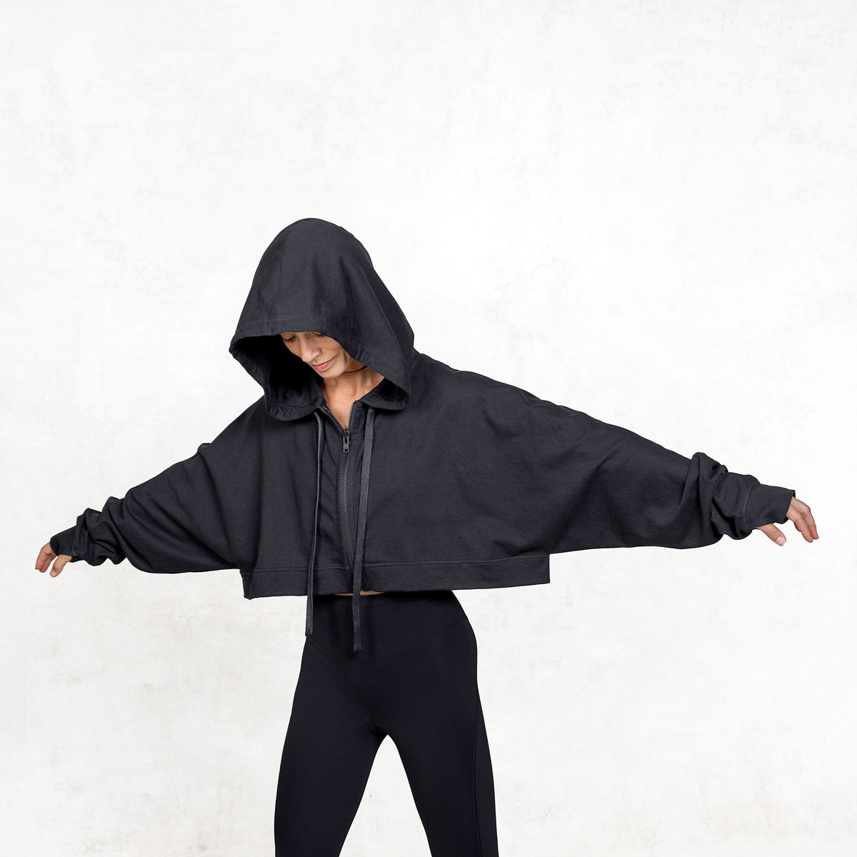 Model shown from the waist up with extended arms, wearing black cropped French terry Daydreamer Hoodie with kimono style sleeves and boxy fit

