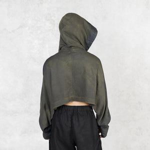 Person facing backward from head to mid-thigh wearing a green and black  cropped hoodie with the hood up against a light gray background