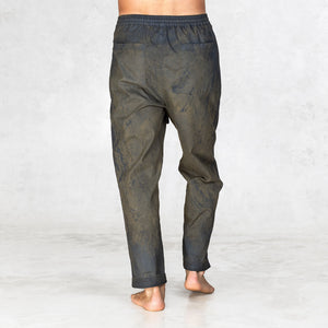 Hand painted half olive half black pants worn by a person shown feet to waist facing backwards on a light gray background