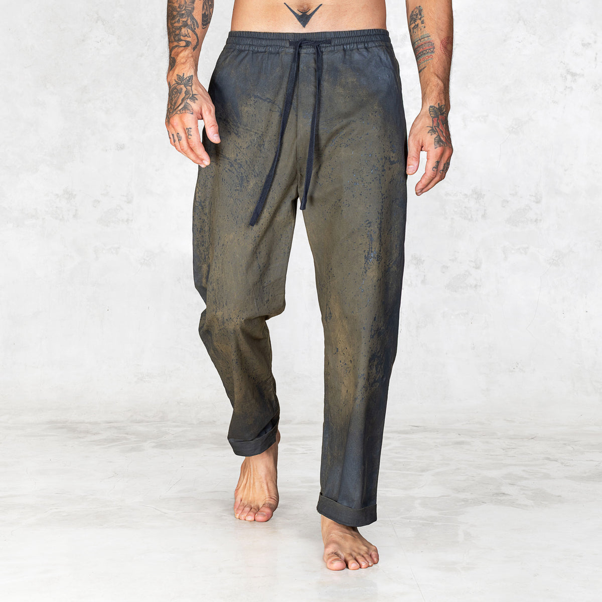 Hand painted half olive half black pants worn by a person shown feet to waist facing forward on a light gray background