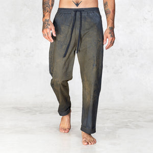 Hand painted half olive half black pants worn by a person shown feet to waist facing forward on a light gray background
