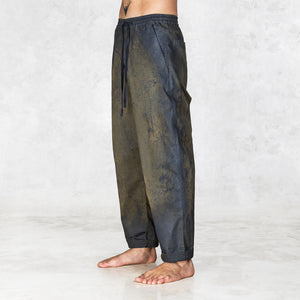 Hand painted half olive half black pants worn by a person shown feet to waist on a light gray background