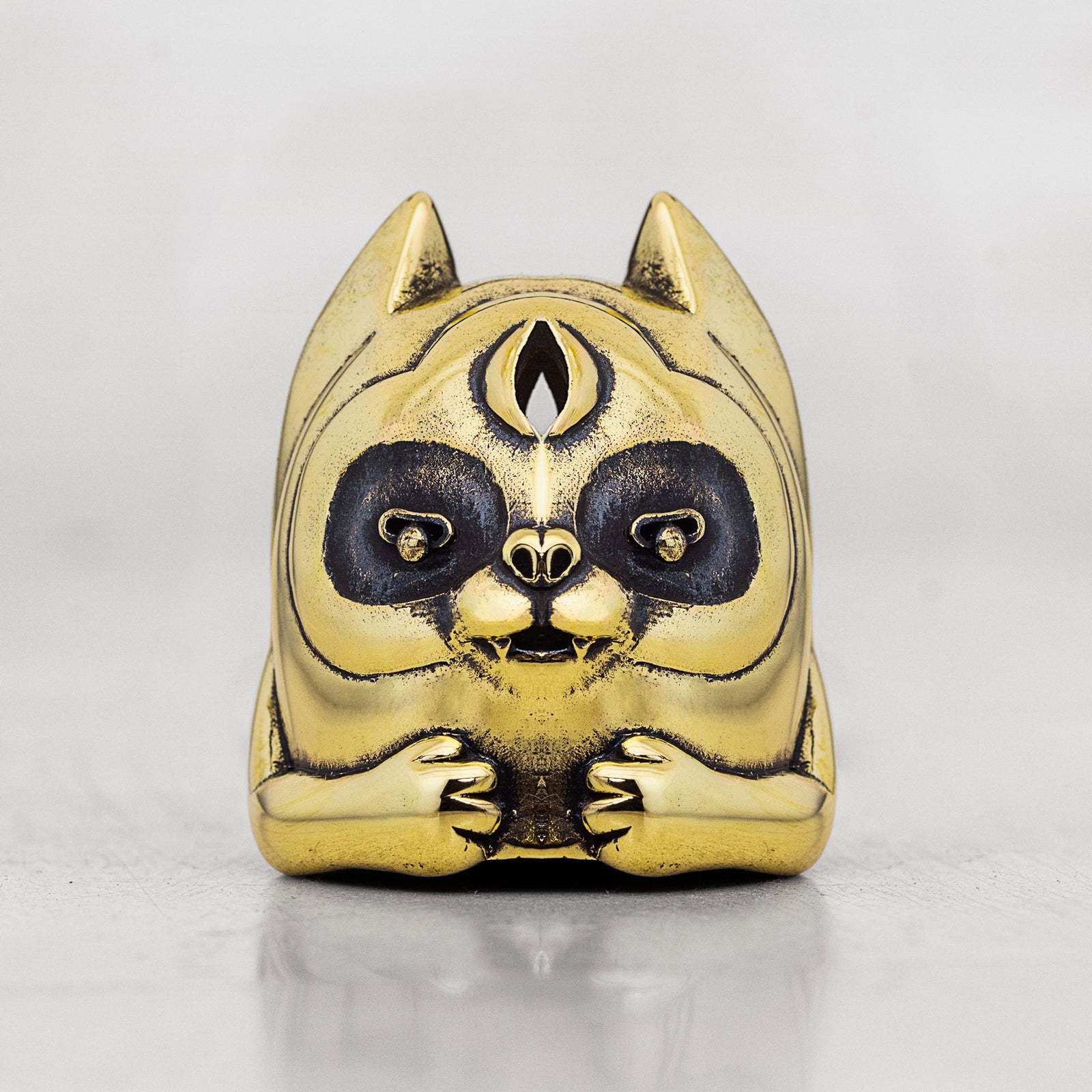 Brass gold and black creature head with paws and pointy ears placed on a white surface