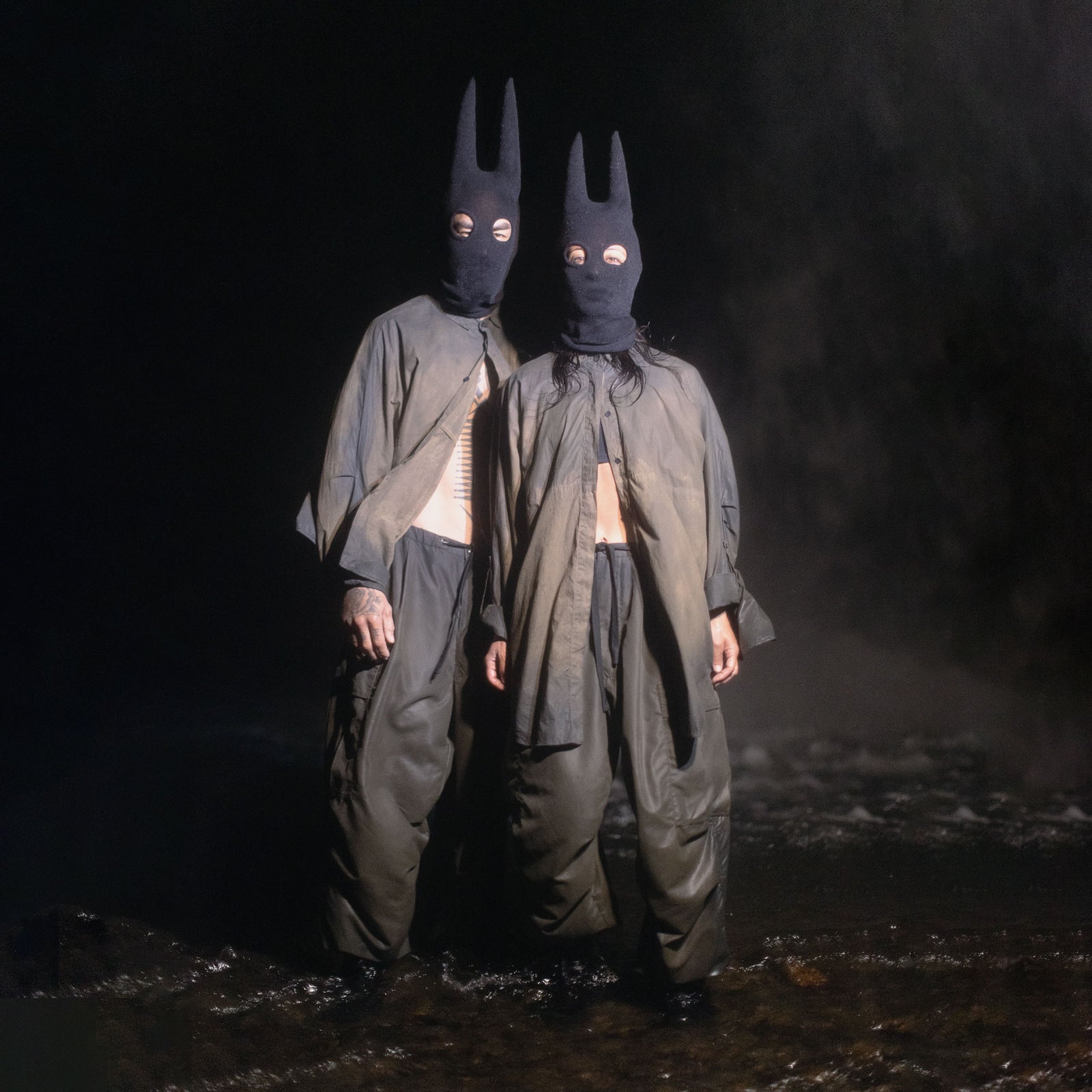 Two people wearing black spire masks and green and black outfits in a dark setting