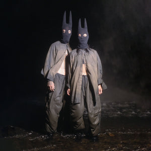 Two people wearing black spire masks and green and black outfits in a dark setting