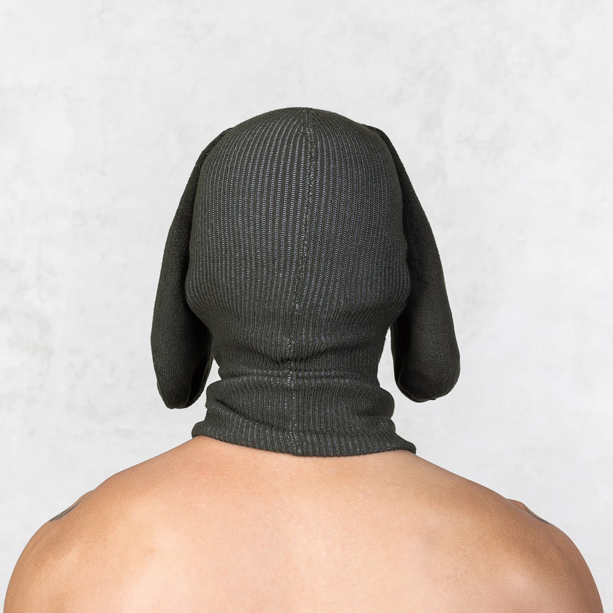Person wearing a dark green knitted dog hood on a light gray background