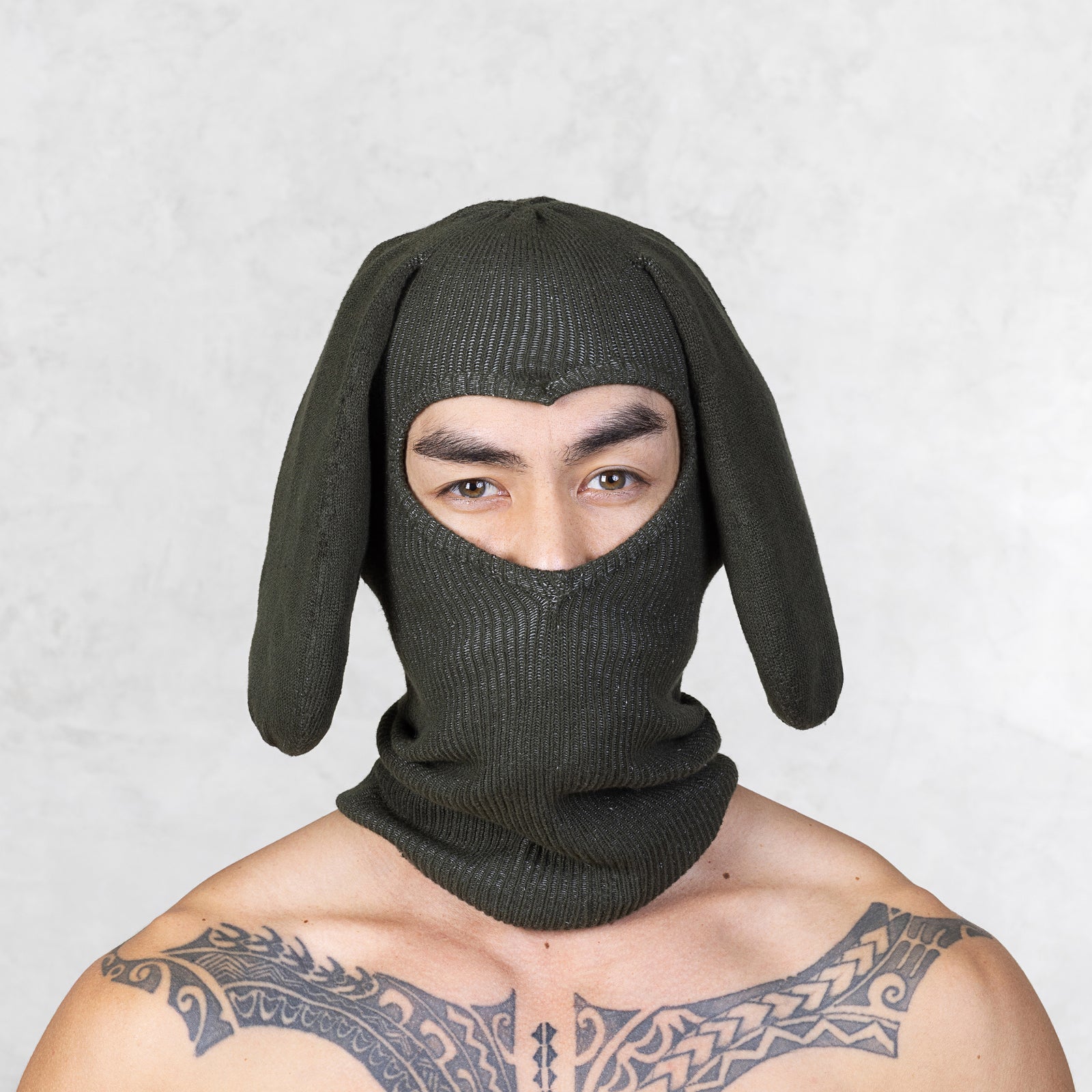Person wearing a dark green bunny mask against a light gray background
