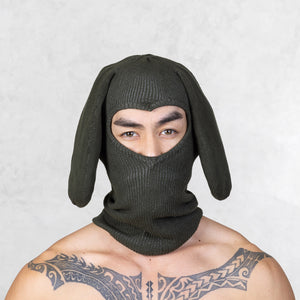 Person wearing a dark green bunny mask against a light gray background
