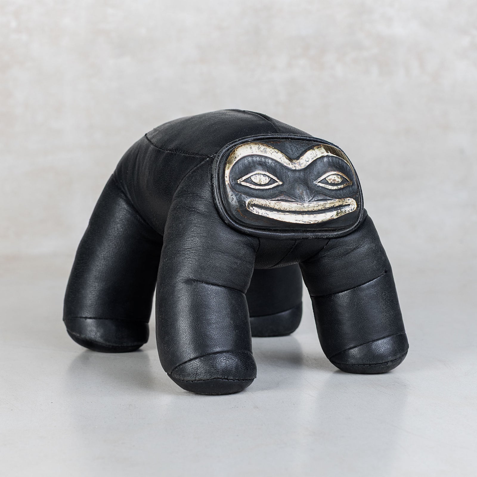 Black leather toy with a brass face design on a light gray background