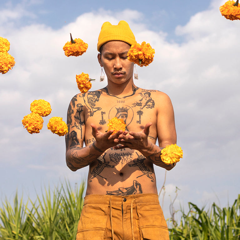 Person with tattoos holding marigold flowers against a blue sky