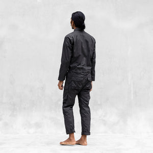 A man standing backwards in a one piece black walnut mechanic style BLAMO jumpsuit 