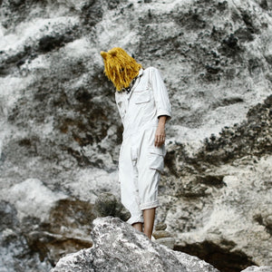 Person in white outfit with yellow hair standing on a rocky surface