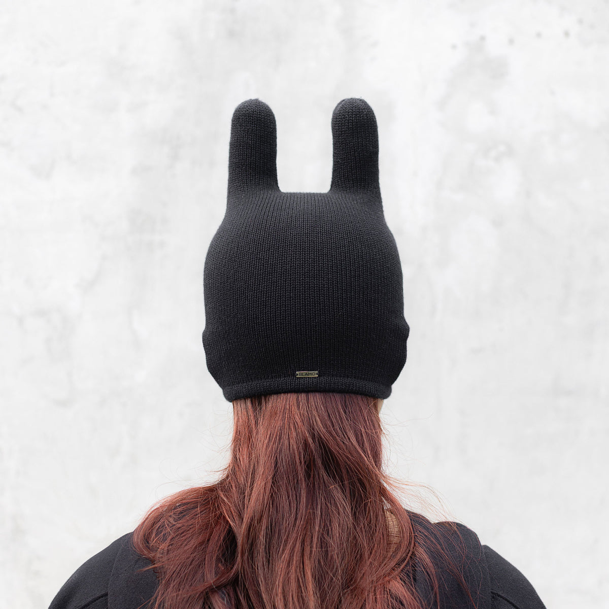 Person facing backwards wearing a black mask with ears on a light gray background