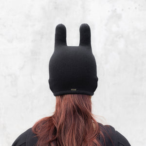 Person facing backwards wearing a black mask with ears on a light gray background