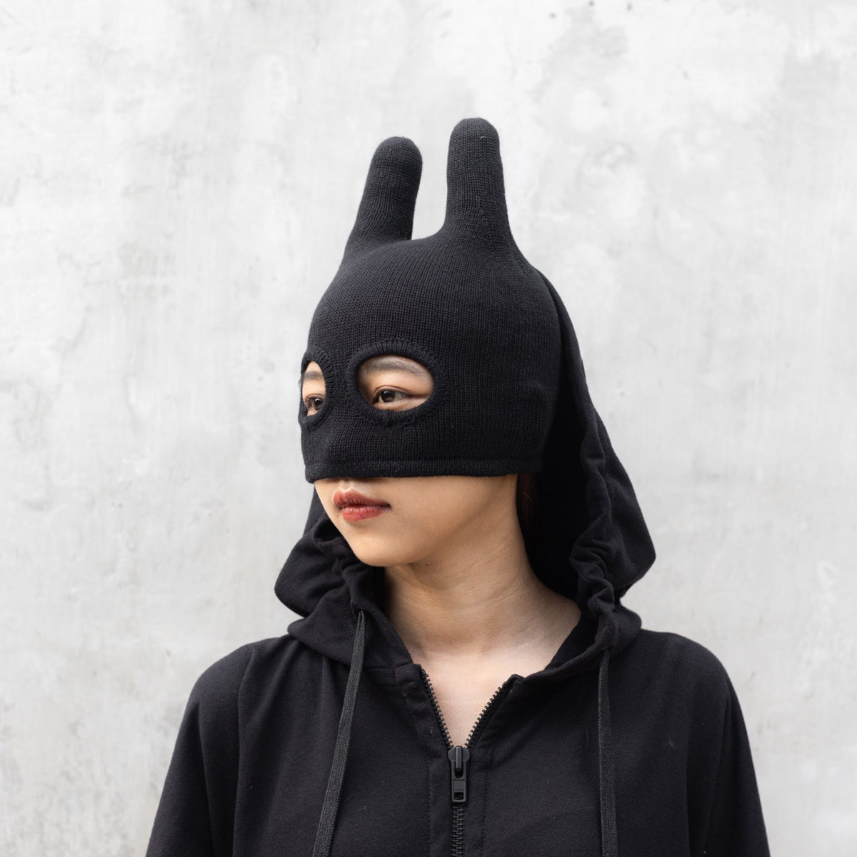 Person wearing a black mask with ears on a light gray background