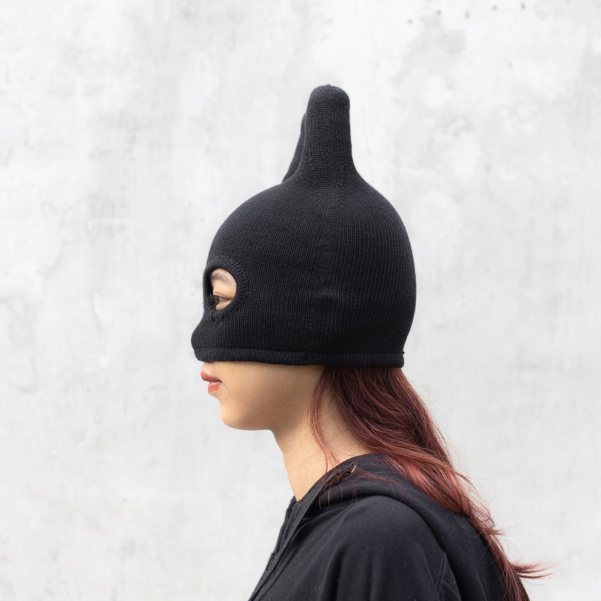 Person facing sideways wearing a black mask with ears on a light gray background