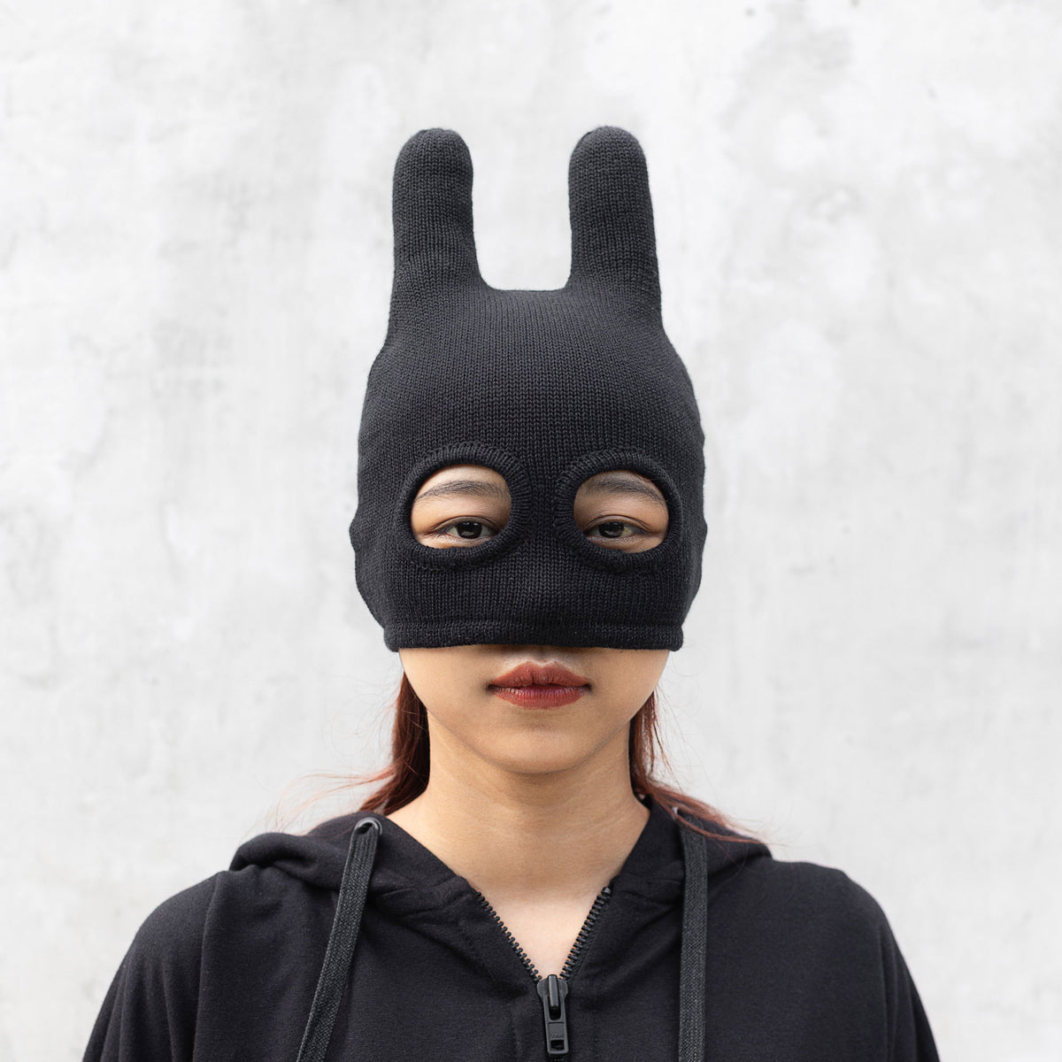 Person wearing a black mask on a light gray background