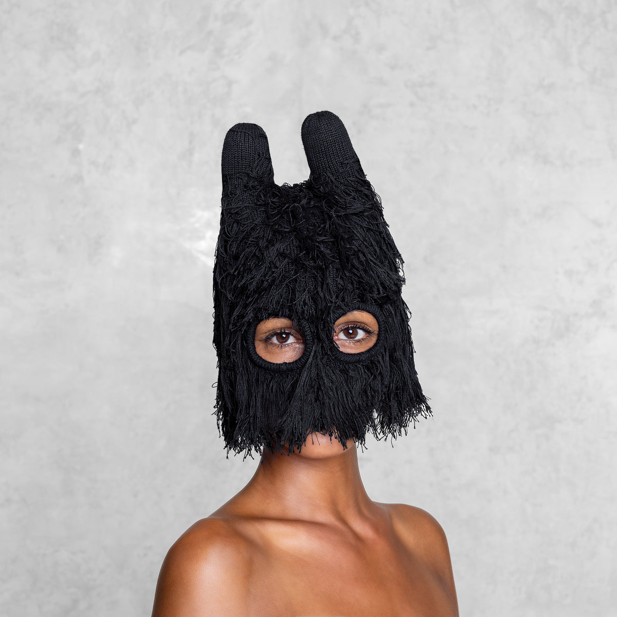 Woman from the chest up wearing a fuzzy black balaclava with horns that is covering half her face. 
