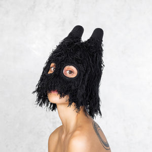 Woman from the chest up wearing a fuzzy black balaclava with horns that is covering half her face. 