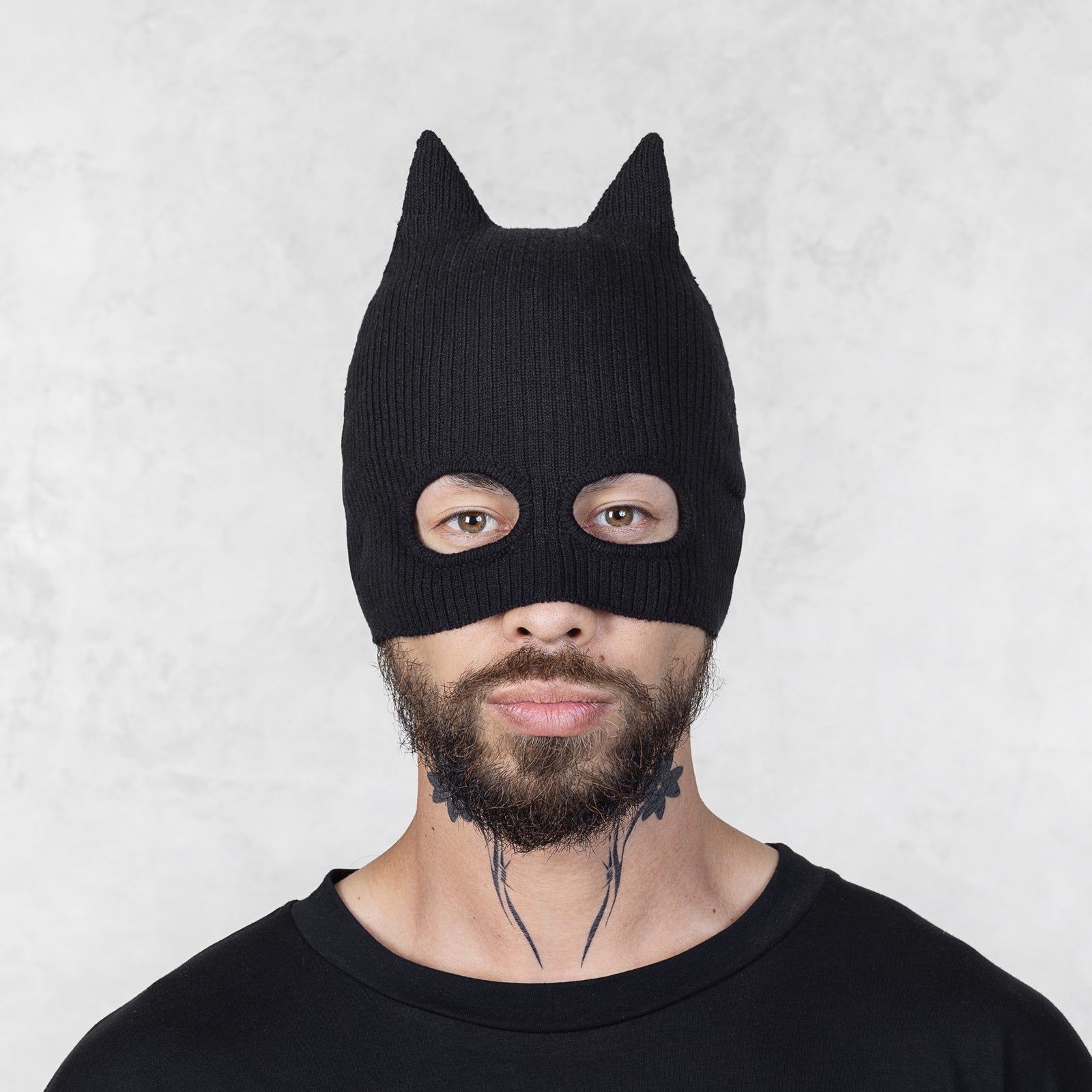 Person wearing a black knit mask with ears on a light gray background