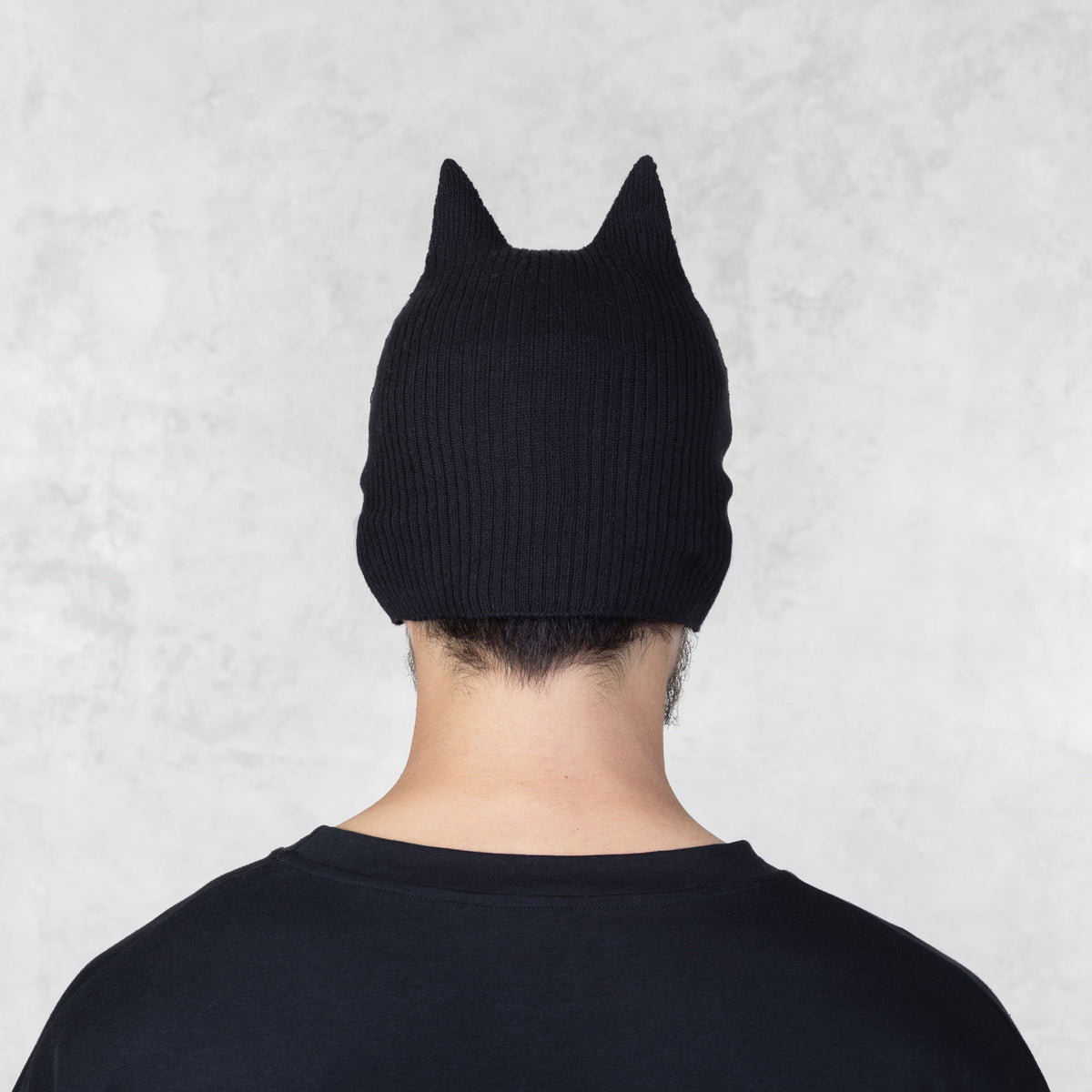 Person wearing a black knit mask with ears facing backwards on a light gray background