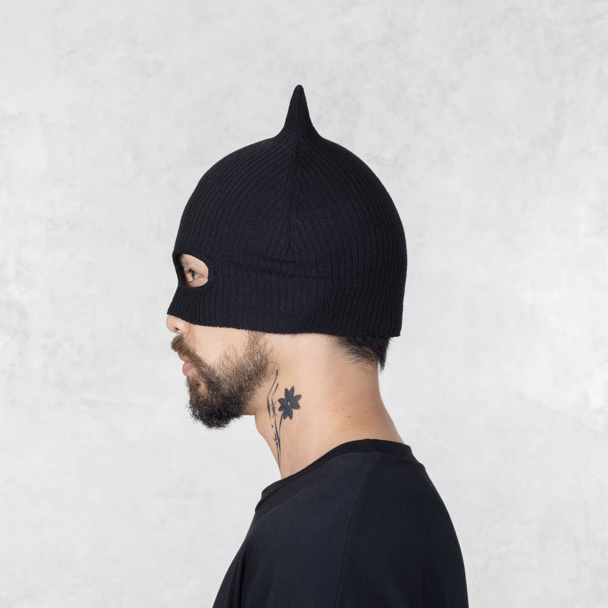 Person wearing a black knit mask with ears facing sideways on a light gray background