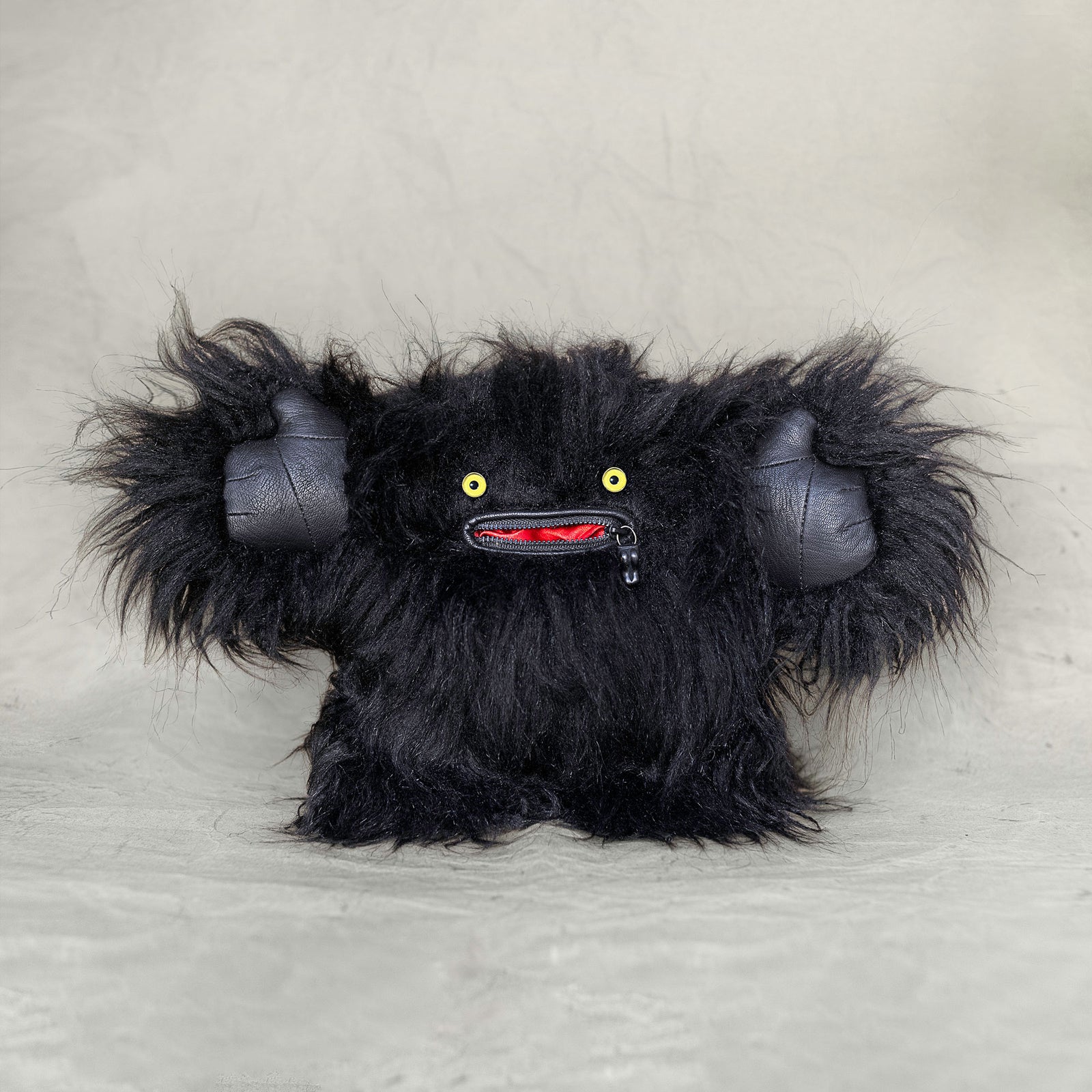 Black furry monster plush toy on a light gray background