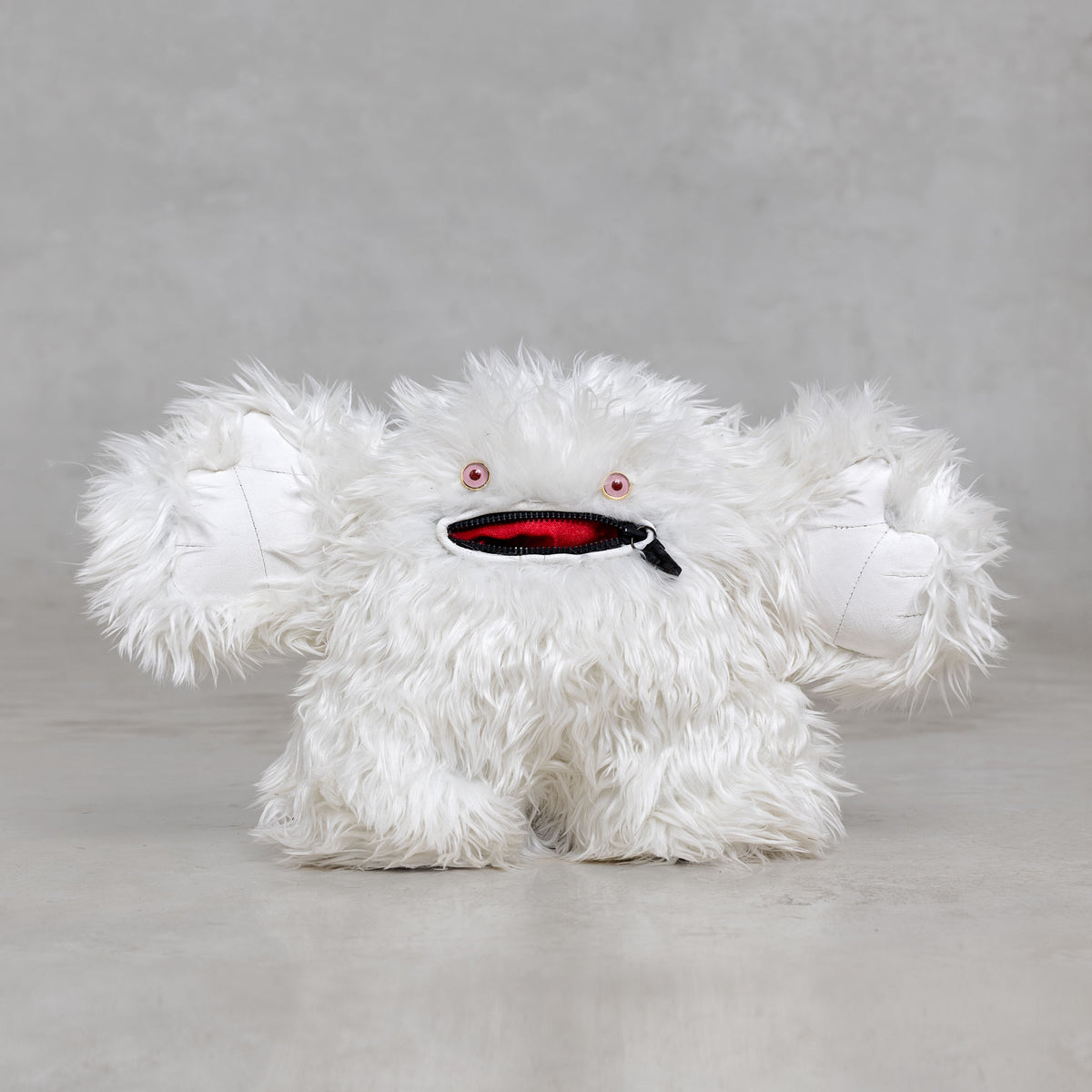 White fluffy creature with pink eyes and a black and red mouth on a gray background