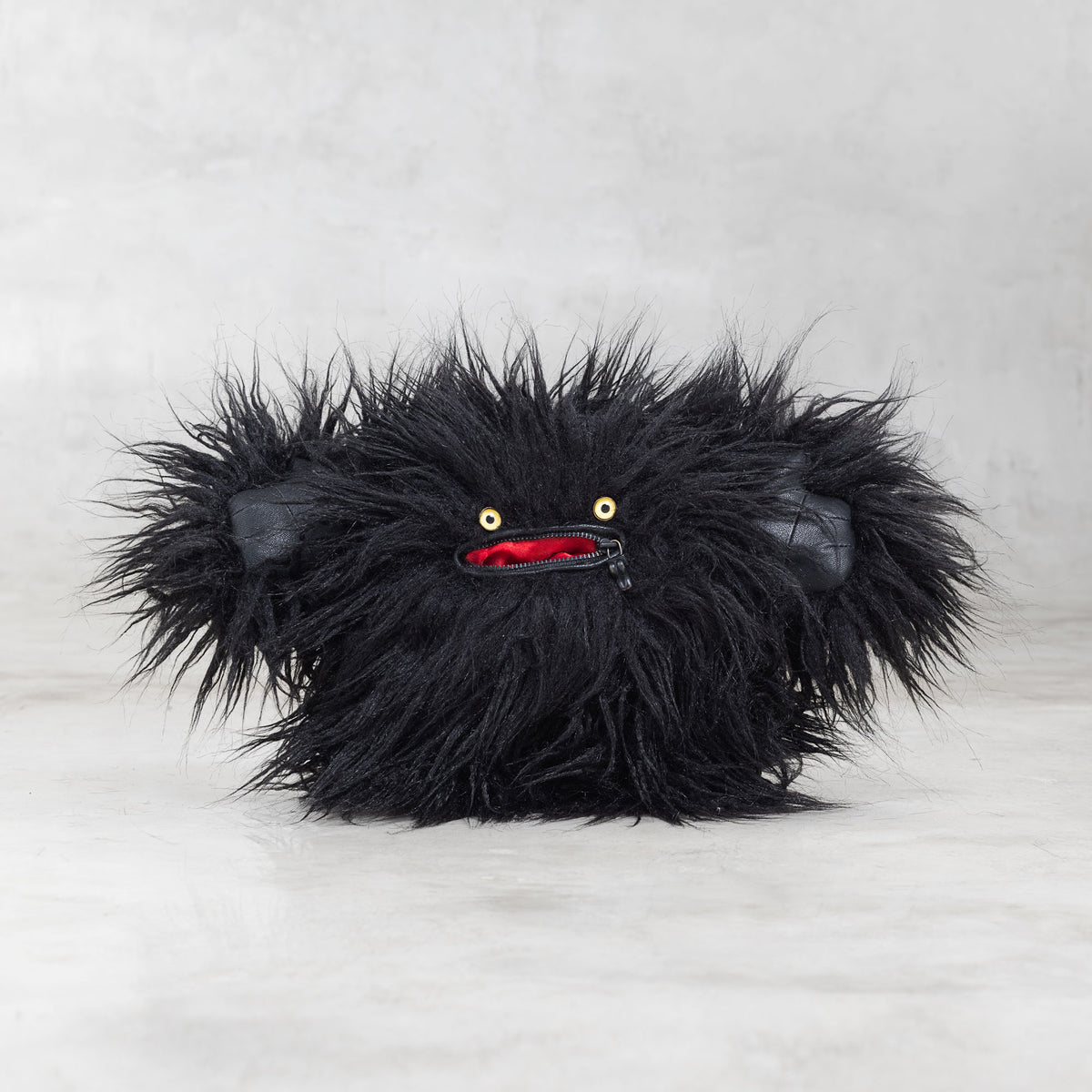 Black furry monster plush toy on a light gray background