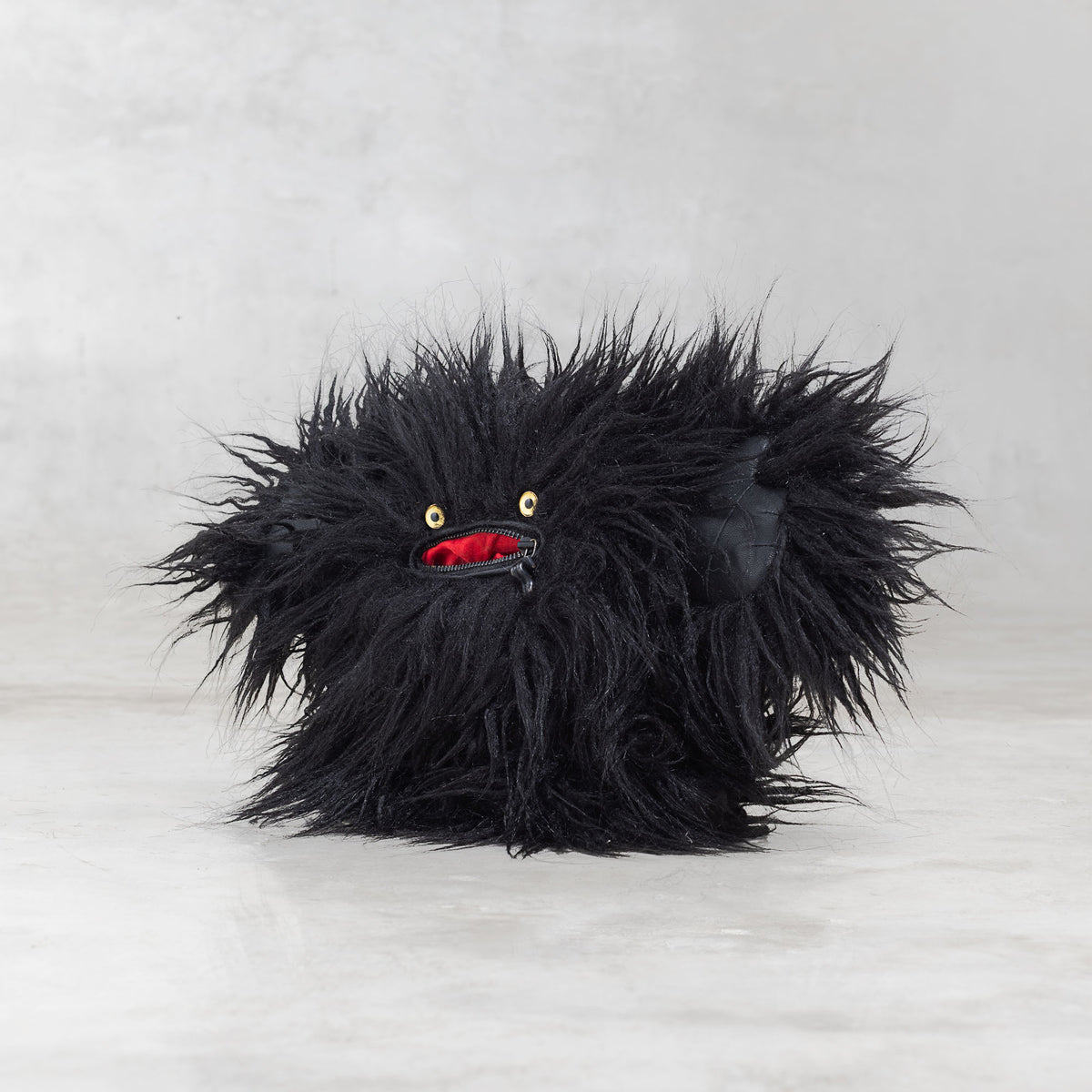 Black furry creature with red mouth and yellow eyes on a light gray background