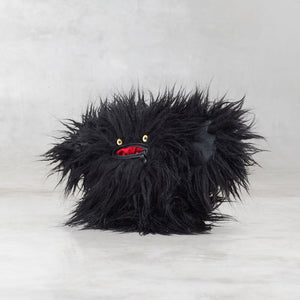 Black furry creature with red mouth and yellow eyes on a light gray background