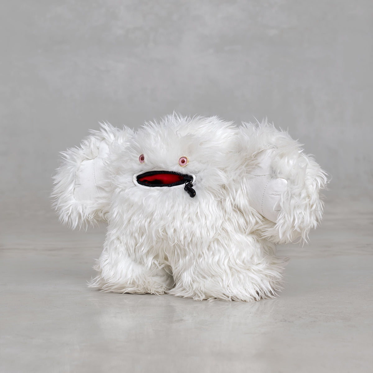 White fluffy creature with pink eyes and a black and red mouth on a gray background