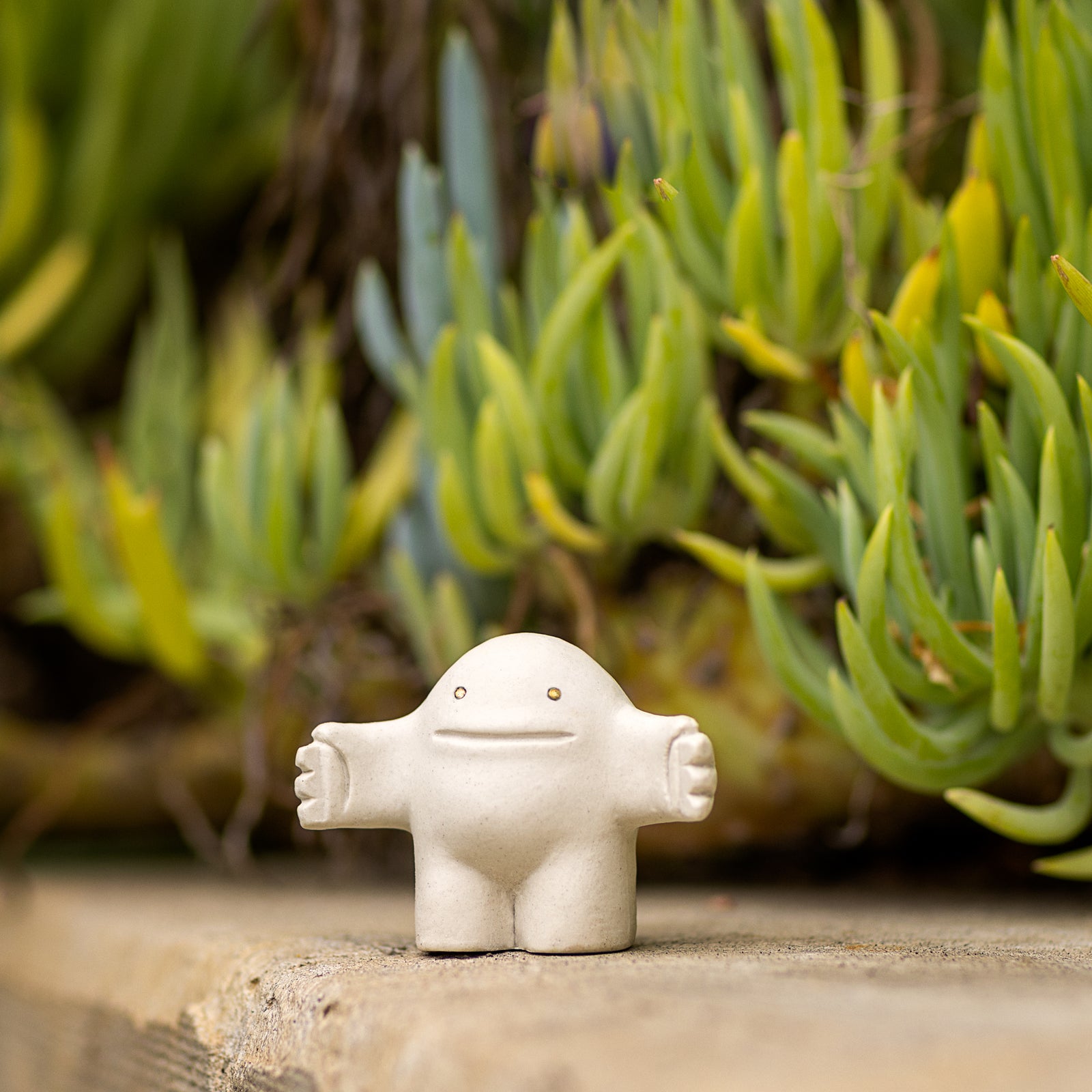 White ceramic figure on a wooden surface with green plants in the background