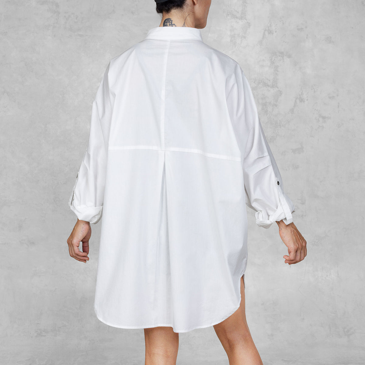 Person facing backwards wearing a white oversized shirt against a gray background