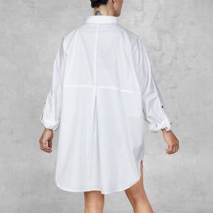 Person facing backwards wearing a white oversized shirt against a gray background