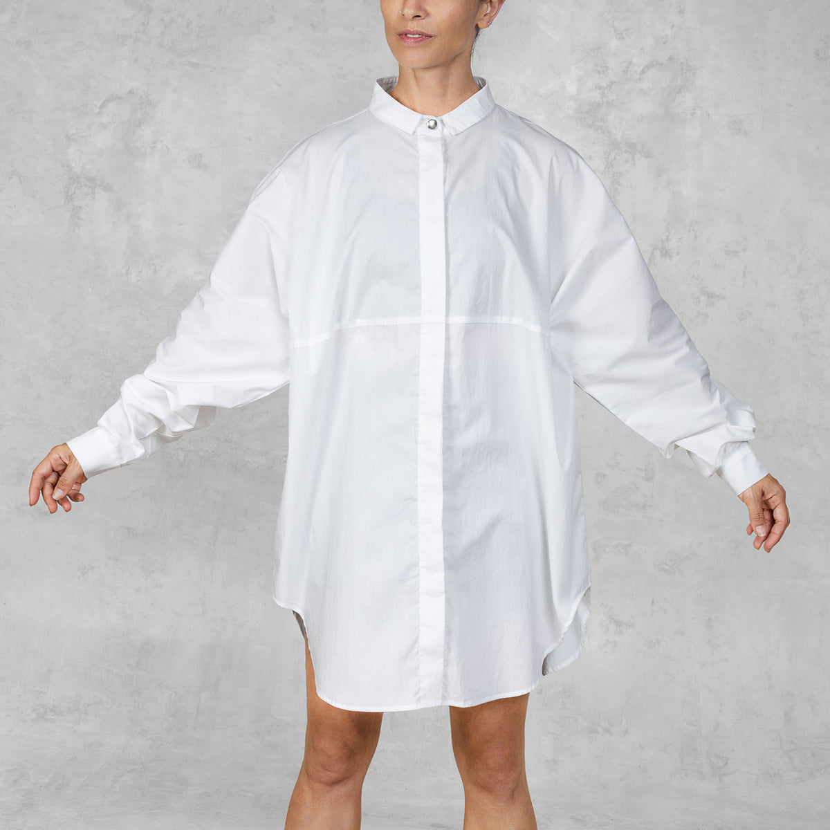 Person wearing a white oversized shirt against a gray background