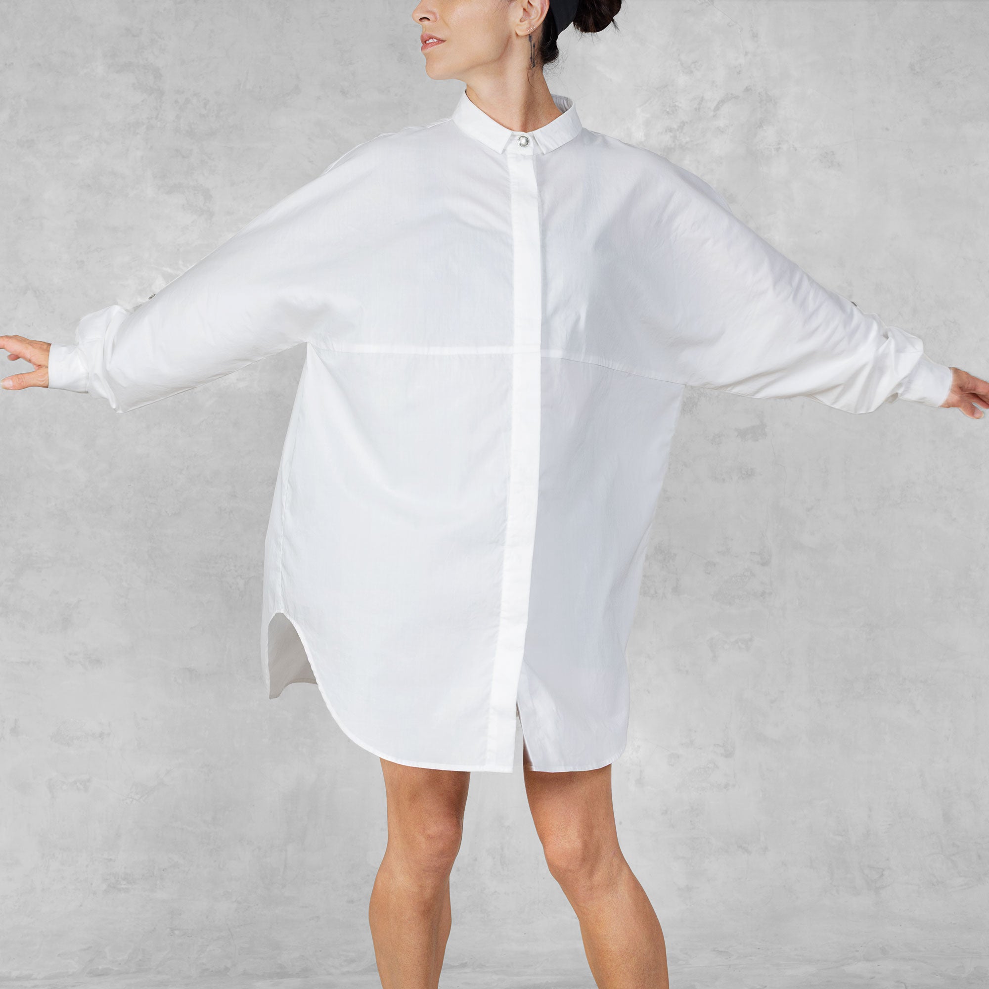 Person with their arms stretched out wearing a white oversized shirt against a plain background