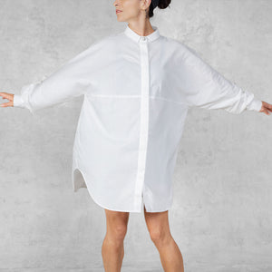 Person with their arms stretched out wearing a white oversized shirt against a plain background