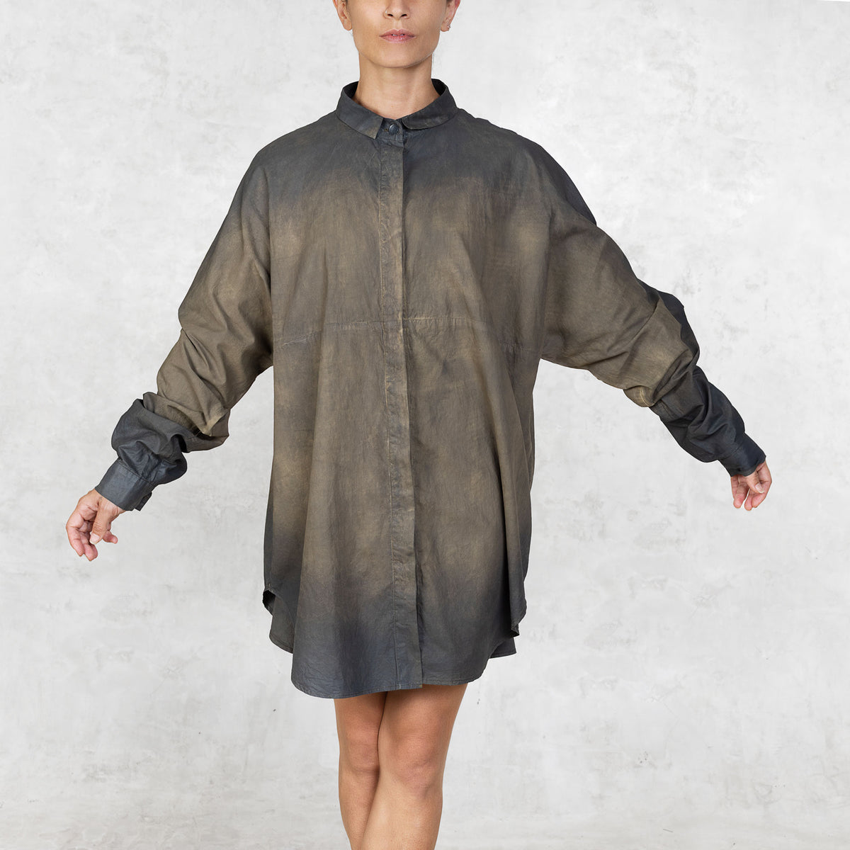 Front facing view of person wearing hand-painted olive tunic button up shirt with arms extended against a white background