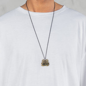 A close-up of a person wearing a white t-shirt and a long black chain necklace with a textured gold pendant.