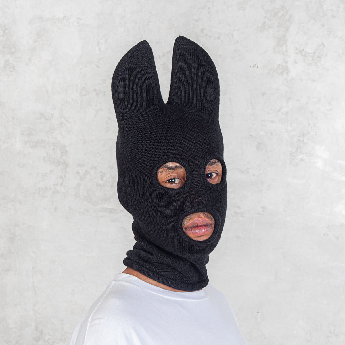 Person wearing a black balaclava with bat ears against a light gray background