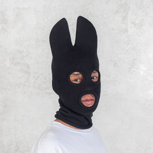 Person wearing a black balaclava with bat ears against a light gray background