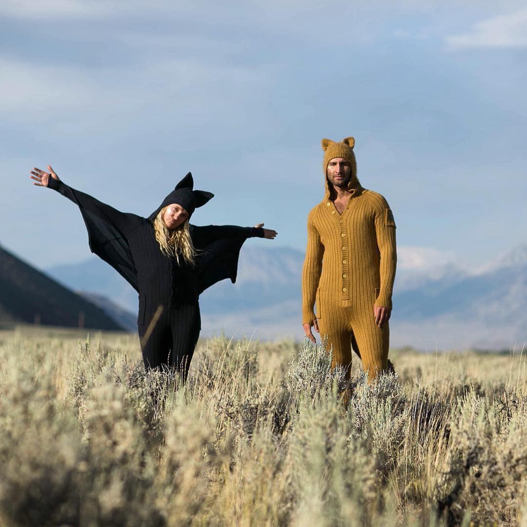 Two people in animal-themed outfits standing in a field with mountains in the background