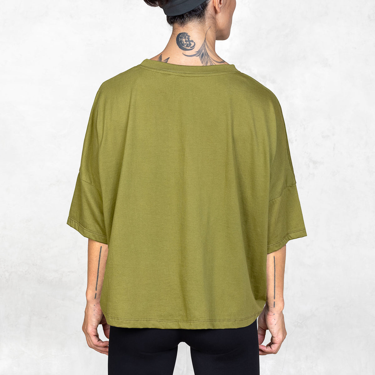 Back facing view of person from mid thigh to nape of neck wearing olive cropped tee in front of a white background