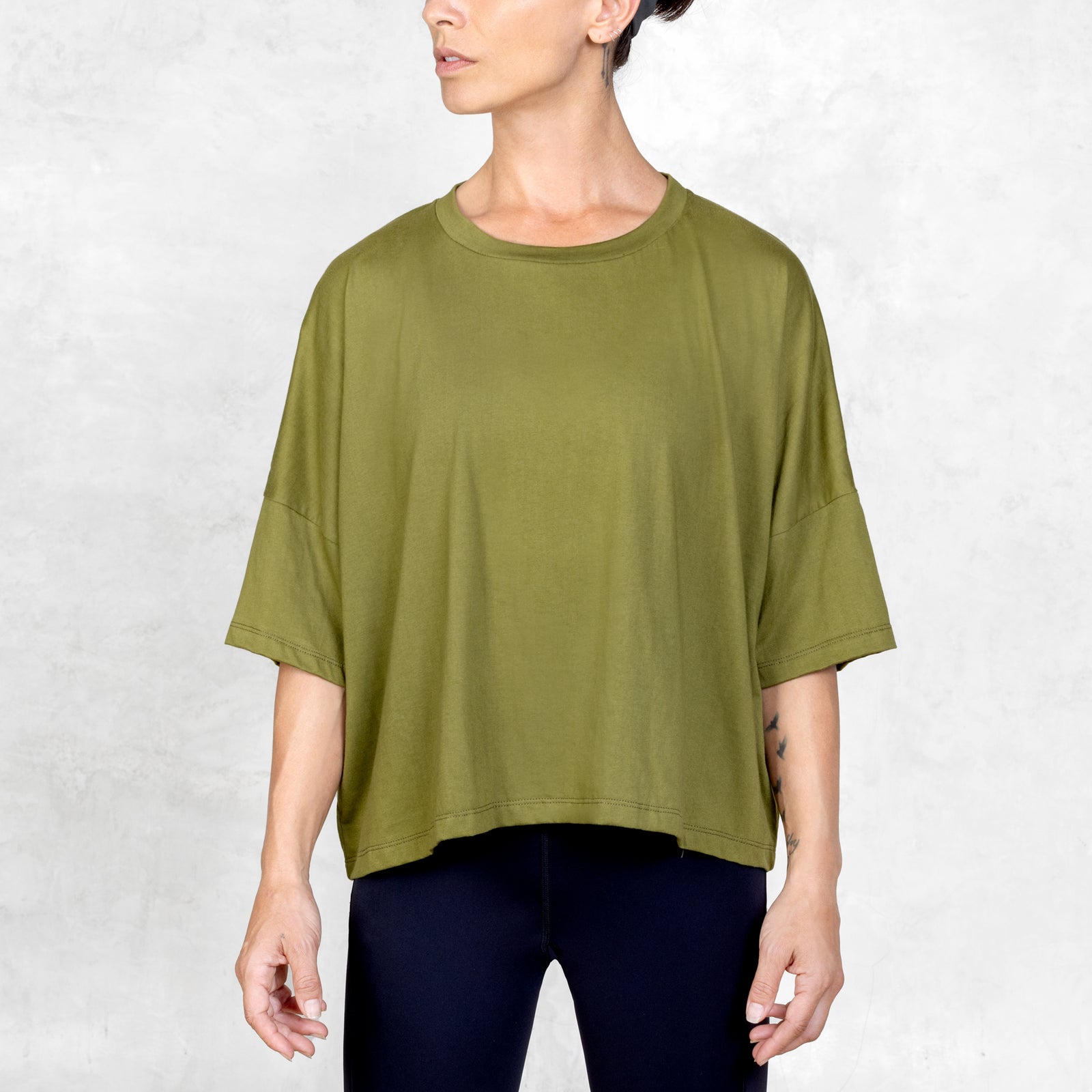Front facing person from mid thigh to neck wearing olive cropped tee in front of a white background