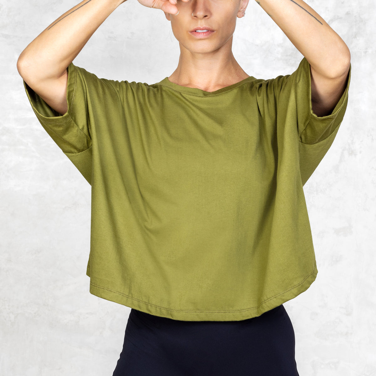 Front facing person from waist to neck wearing olive cropped tee in front of a white background