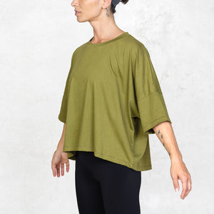 side view of person from mid thigh to neck wearing olive cropped tee in front of a white background